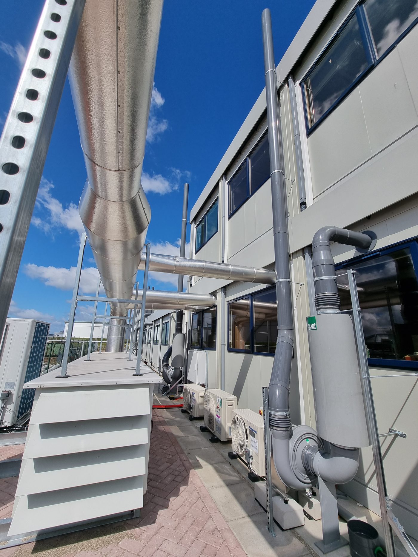 Afzuigunits met dempers, slakkenhuisventilatoren en leidingen langs het gebouw