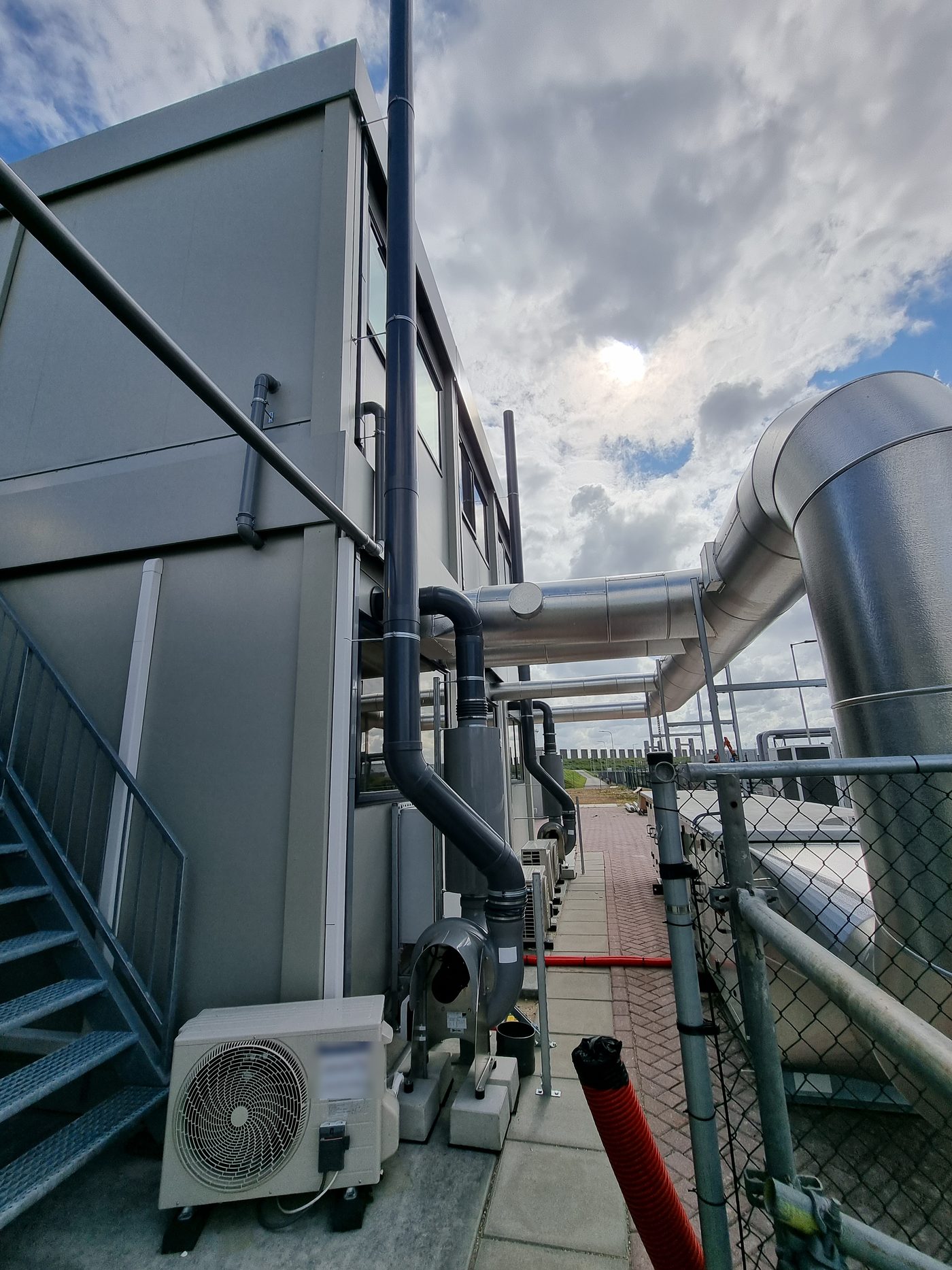Uitblaasleiding en ventilator langs de gevel van het laboratorium