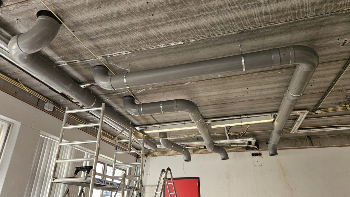 PVC-leidingen onder het plafond van een lokaal, op weg naar de dakdoorvoer