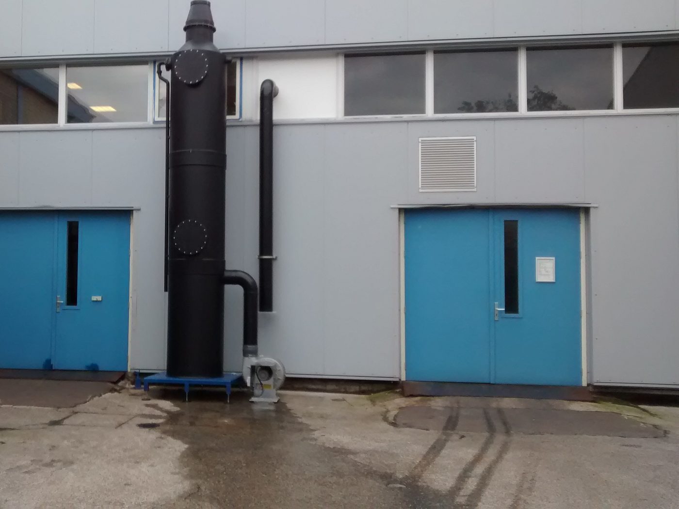 Gaswasser bij de blauwe deuren van het gebouw, met ventilator en leidingwerk