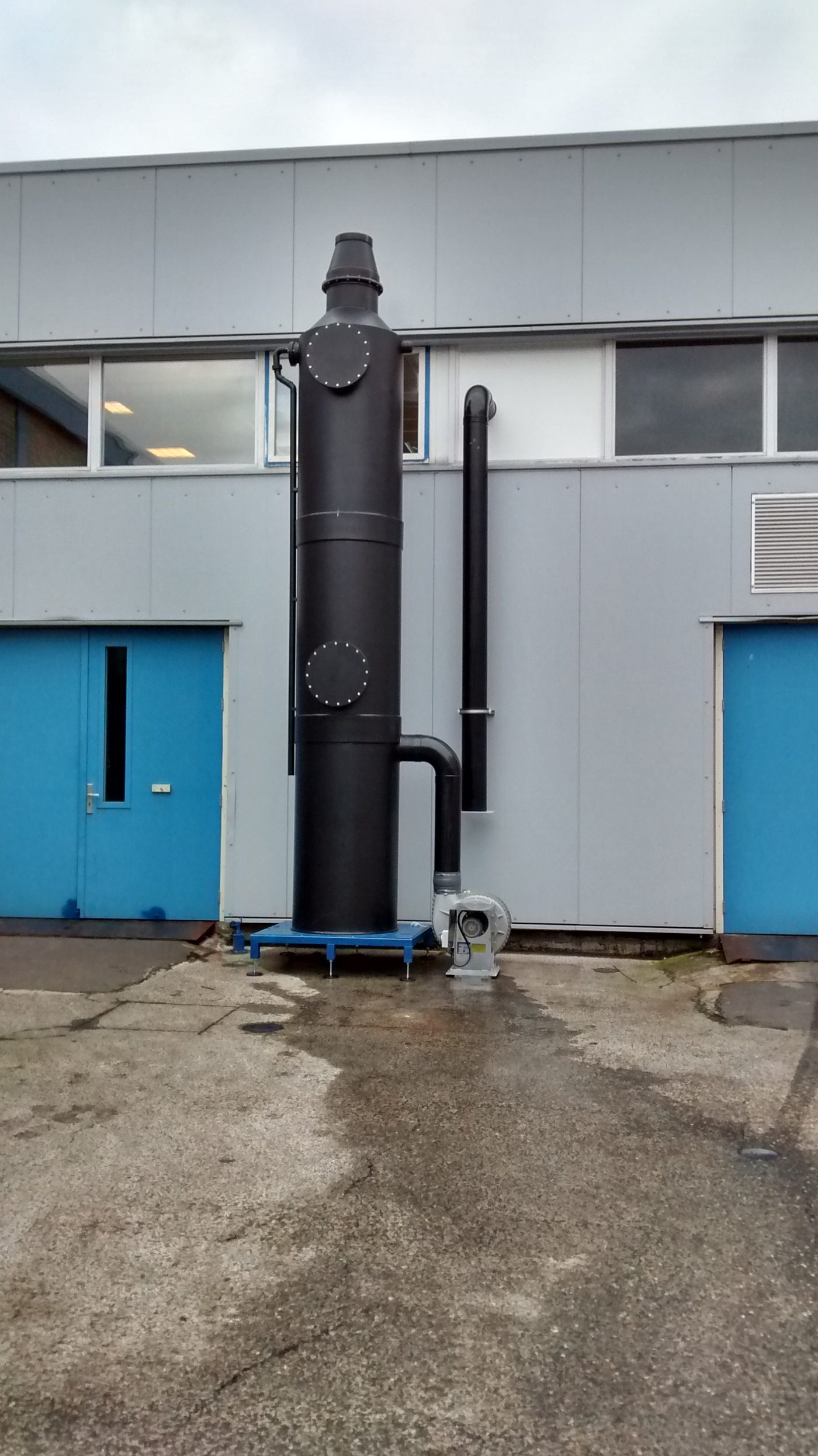 Kleine gaswasser van zwart kunststof tegen een gevel, met ventilator en afvoerleiding